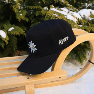 Schwarze Alpsnow Snapback Cap mit Edelweiß-Stick auf einem Holzschlitten im Schnee