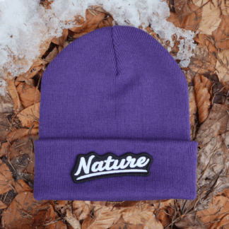Alpsnow Mütze in intensivem Lila mit einem geschwungenen, weißen "Nature" Patch auf dem Umschlag, liegend auf Laub und Schnee. 🏔️
