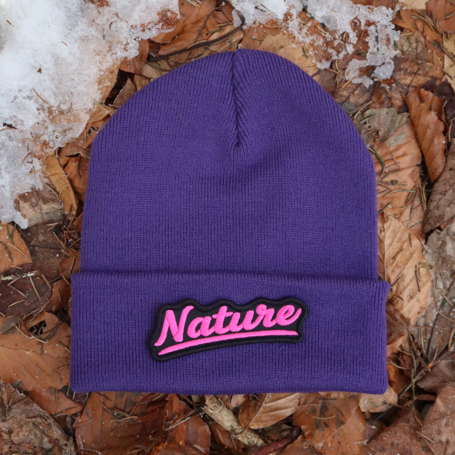 Alpsnow Mütze in intensivem Lila mit einem geschwungenen "Nature" Patch, der pink gestickt ist, auf dem Umschlag, perfekt für einen Pop-of-Color-Look. 🏔️