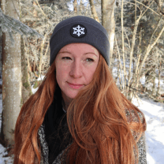 Alpsnow Mütze in modernem Grau mit einem runden, weißen Eiskristall Patch auf dem Umschlag, getragen von einer Person im Schnee.