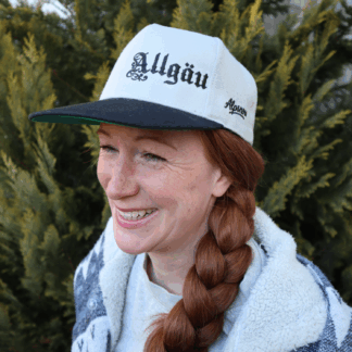 Frau mit rotem Zopf trägt die hellgraue Alpsnow Snapback Cap mit schwarzem Schirm und Allgäu-Stick