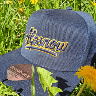 Navyblaue Alpsnow Snapback mit goldenem 3D-Logo im Gras liegend