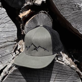 Olivgrüne Alpsnow Trucker Cap mit schwarzem Berg-Stick und schwarzem Mesh auf Holz