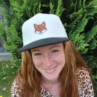 Beige Alpsnow Cap mit Fuchs-Stick und schwarzem Schirm auf einer rustikalen Holzbohle im Freien